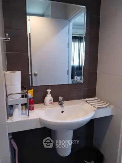Modern bathroom with sleek sink and mirror, featuring essential toiletries and dark tile accents.