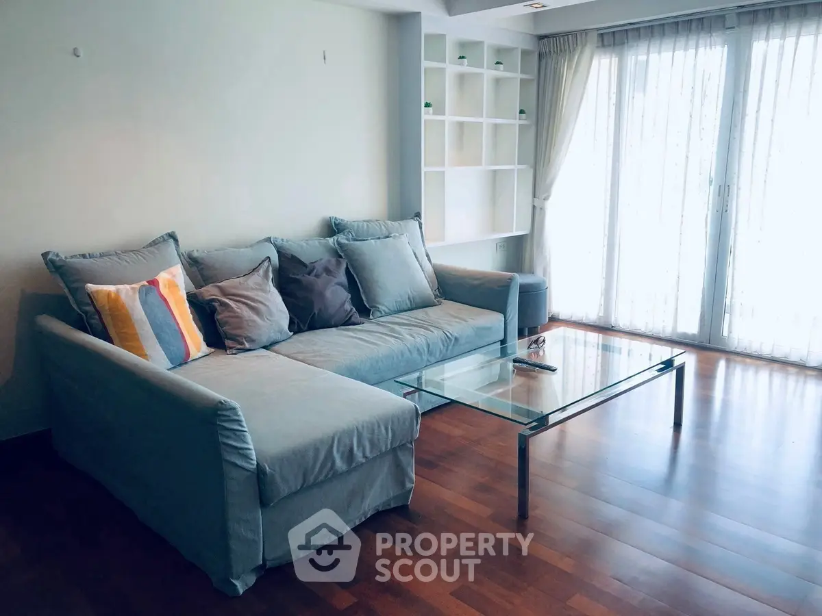 Spacious living room with cozy sofa and glass coffee table, featuring elegant wooden flooring and natural light.