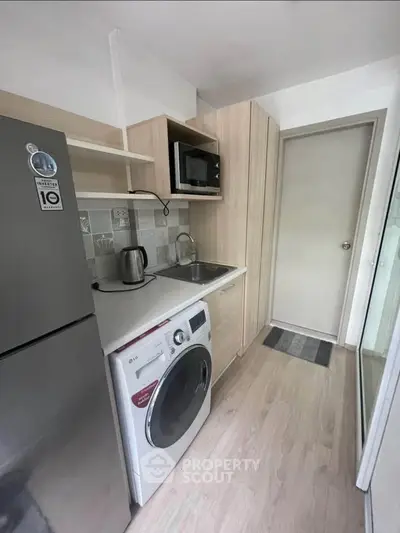 Modern compact kitchen with washing machine and microwave in sleek apartment.