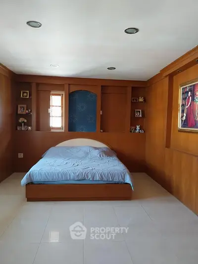 Spacious bedroom with wooden paneling and built-in shelves, featuring a cozy bed and elegant decor.