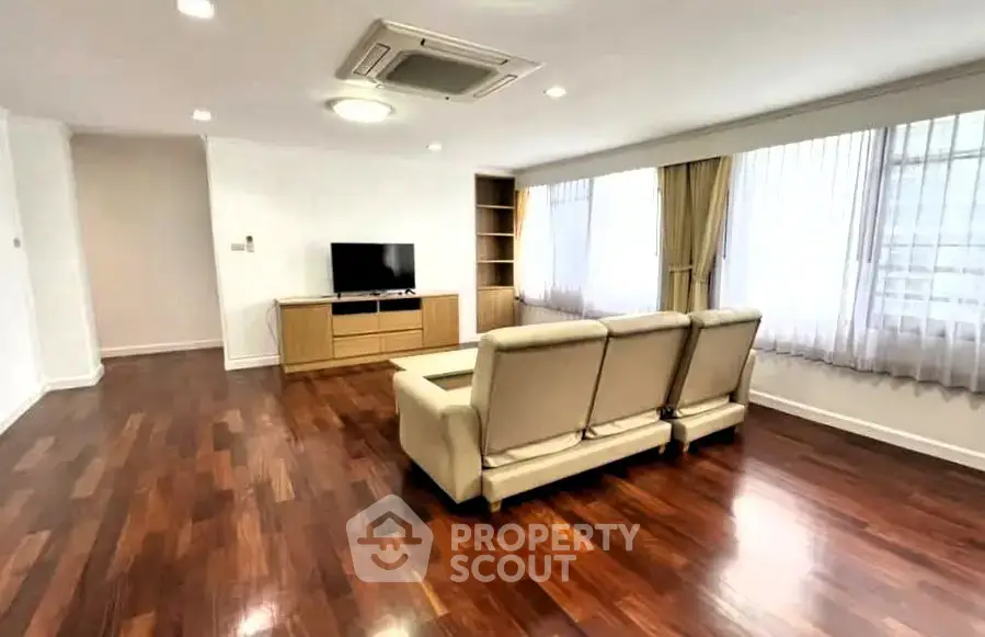 Spacious living room with hardwood floors and modern furnishings in a bright apartment.
