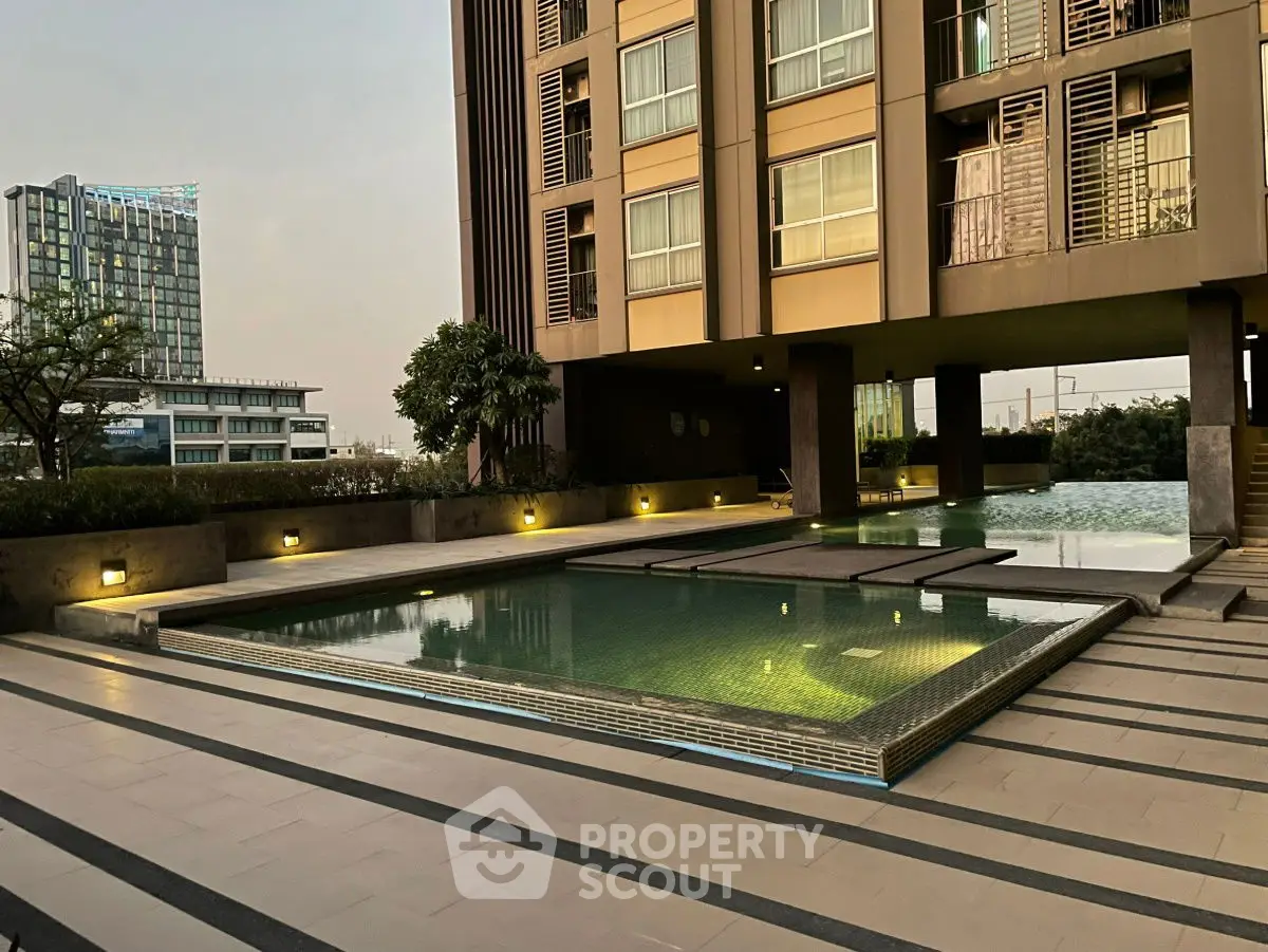 Luxurious modern apartment building with serene poolside view at sunset.