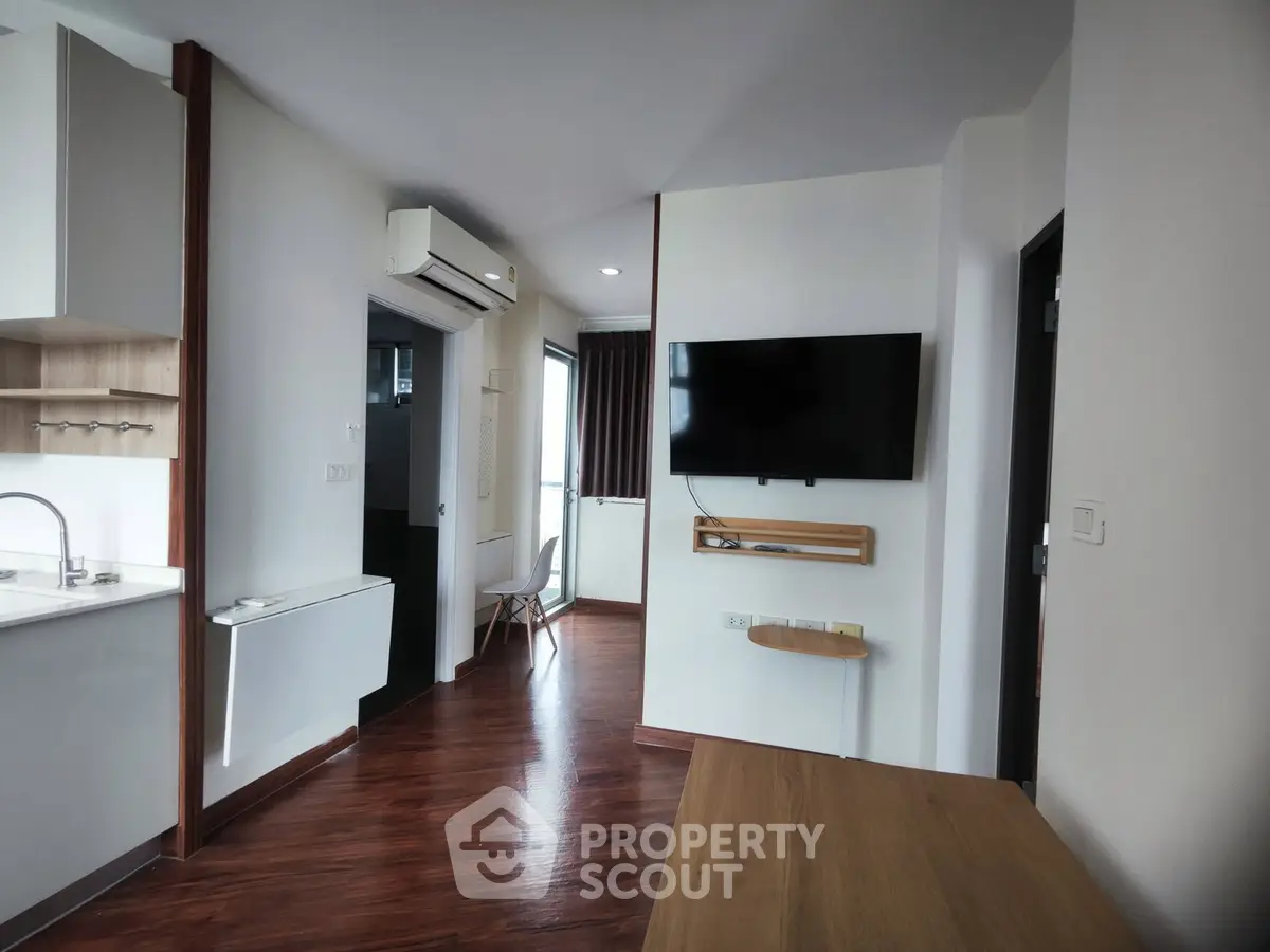 Modern apartment interior with sleek wooden flooring and wall-mounted TV, featuring a compact kitchen area.