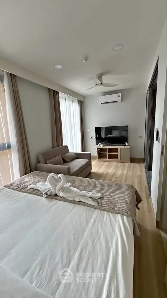 Modern bedroom with cozy seating area and TV, featuring elegant decor and natural light.