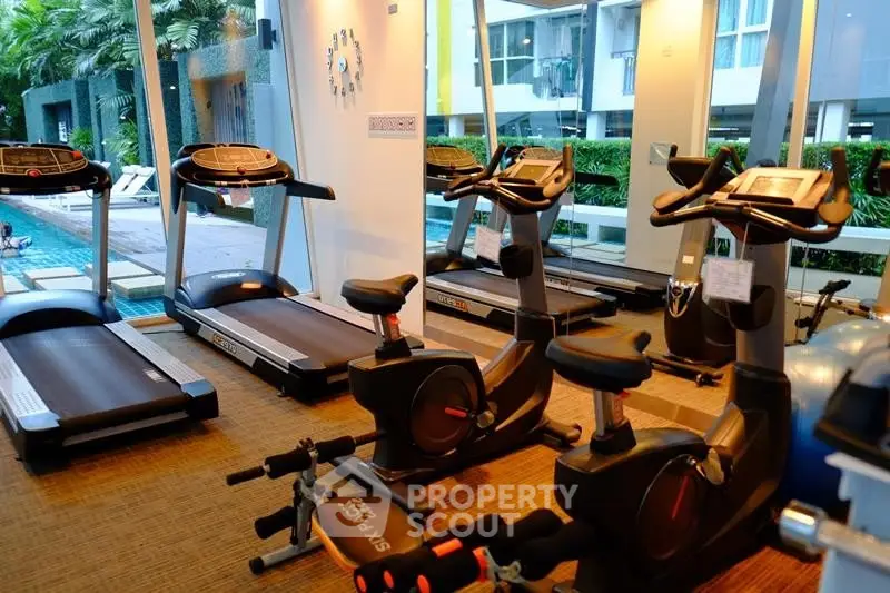 Modern gym with treadmills and exercise bikes overlooking a pool in a luxury apartment complex.