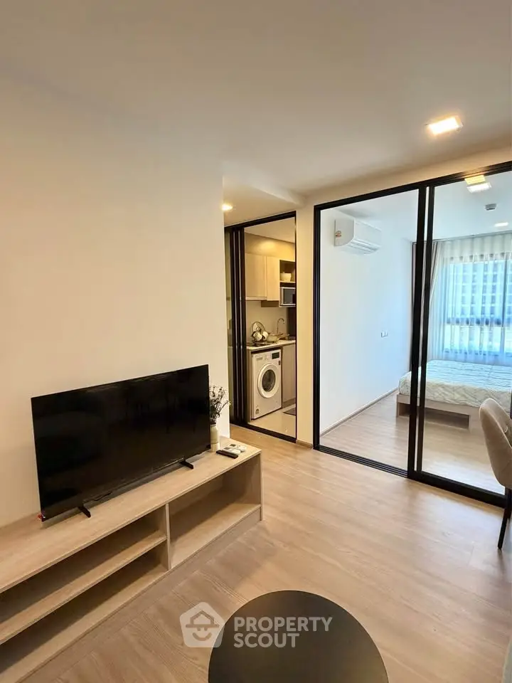 Modern apartment interior with open living room, kitchen, and bedroom view.