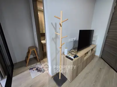 Modern living room with wooden TV stand and coat rack, adjacent to a bathroom entrance.