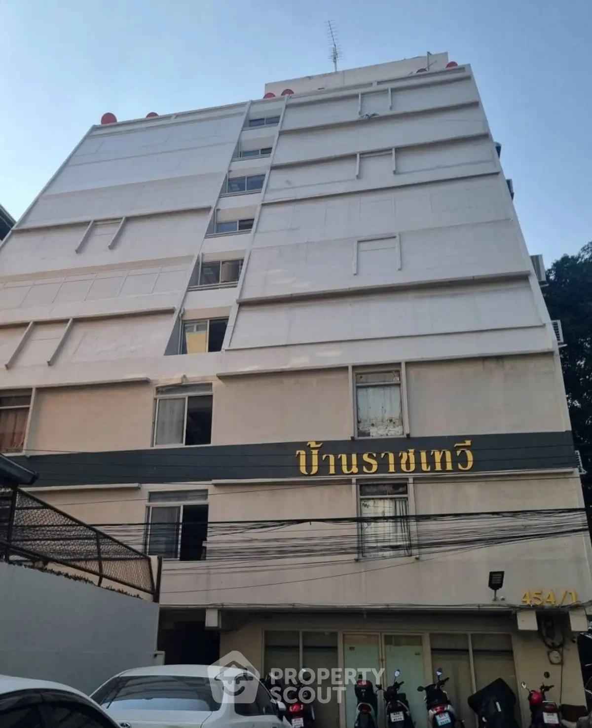 Modern multi-story residential building with parking area and motorbikes in front.