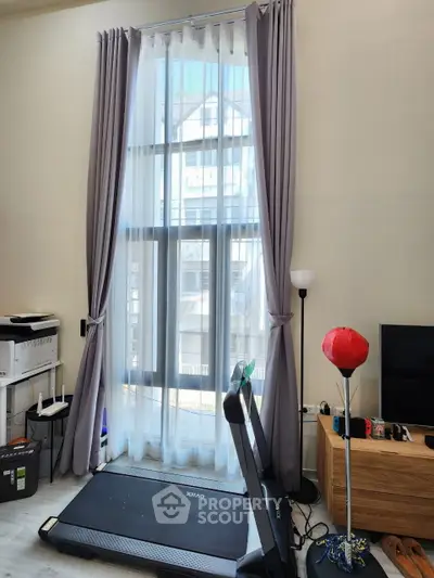 Modern living room with tall windows, treadmill, and entertainment setup in a stylish apartment.