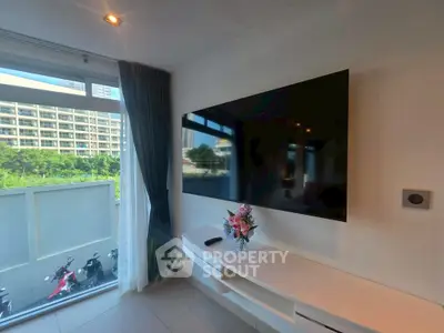Modern living room with large TV and city view, featuring sleek furniture and natural light.