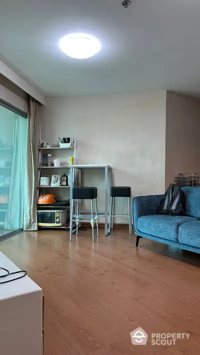 Cozy living space with modern blue sofa, wooden flooring, and a compact dining area with a stylish oven, perfect for urban living.