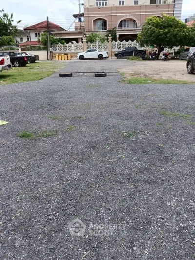 Spacious gravel parking area in residential neighborhood with multiple parked cars and lush greenery.