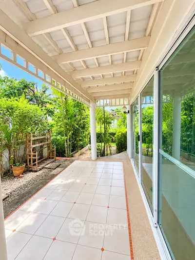 Spacious tiled balcony with lush garden view and large glass doors in a serene setting.