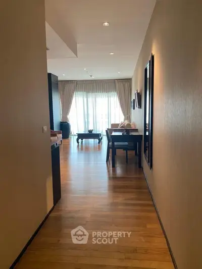 Spacious hallway leading to a bright living area with wooden flooring and elegant decor.