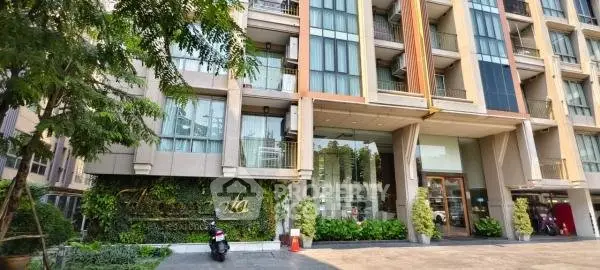 Modern condominium entrance with lush greenery and sleek design in urban setting.