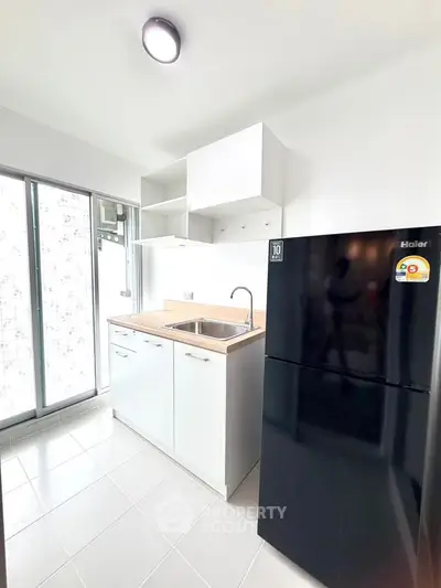 Modern kitchen with sleek black fridge and white cabinetry, featuring a compact open layout and natural light.