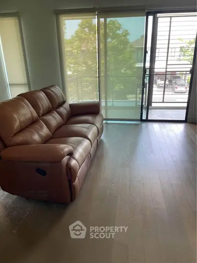 Spacious living room with leather sofa and large windows opening to a balcony view.