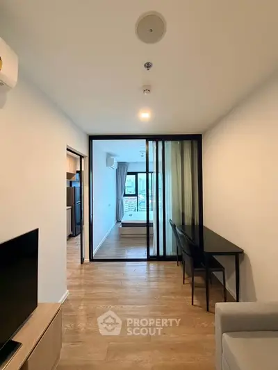 Modern apartment interior with sliding glass doors and wooden flooring, featuring a cozy living area and a glimpse of the bedroom.