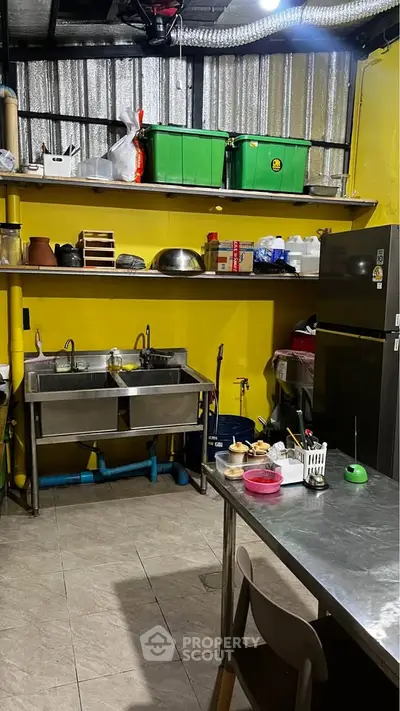 Industrial-style kitchen with stainless steel sink and shelving, vibrant yellow walls, and modern appliances.