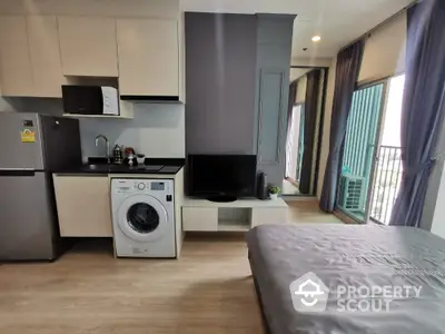 Modern studio apartment with compact kitchen and washing machine, featuring a balcony with city view.