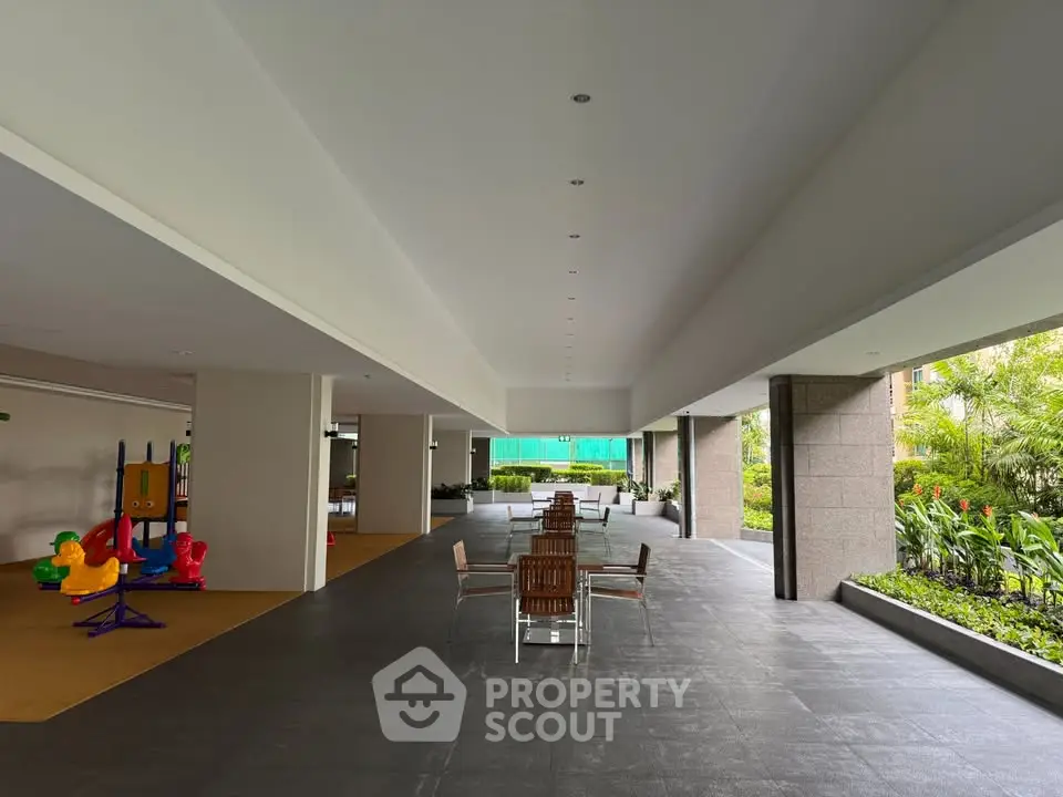 Spacious modern building entrance with seating and children's play area, surrounded by lush greenery.