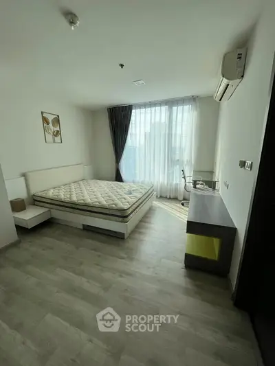 Spacious bedroom with large window and modern furnishings in a stylish apartment.