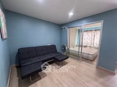 Modern living room with sleek black sofa and sliding glass doors leading to a cozy bedroom.