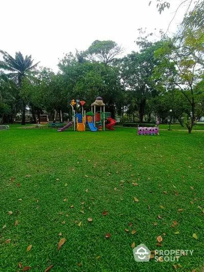 Spacious green park with colorful children's playground equipment and lush trees