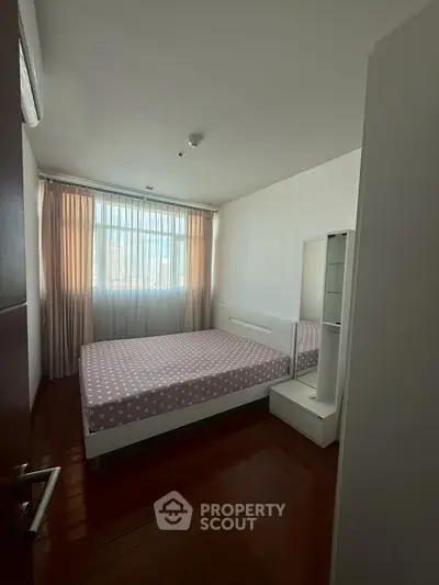 Cozy bedroom with natural light and elegant curtains, featuring a comfortable bed and sleek wooden flooring.