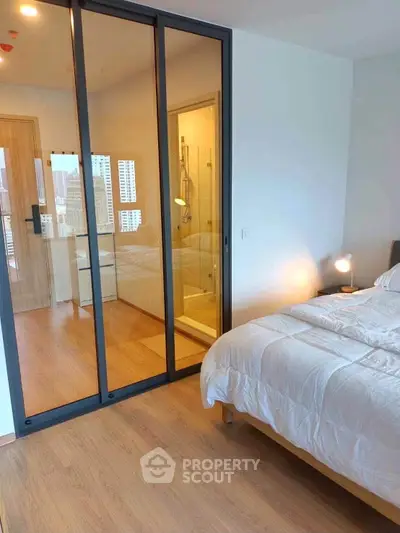 Modern bedroom with glass partition and city view, featuring cozy bedding and wooden flooring.
