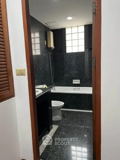 Elegant bathroom with black marble tiles and bathtub in modern home.