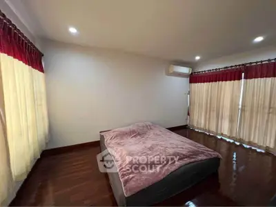 Spacious bedroom with hardwood floors and large windows with red curtains.