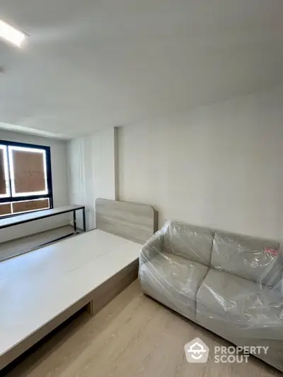 Modern bedroom with minimalist design featuring a bed and sofa, ample natural light from large window.