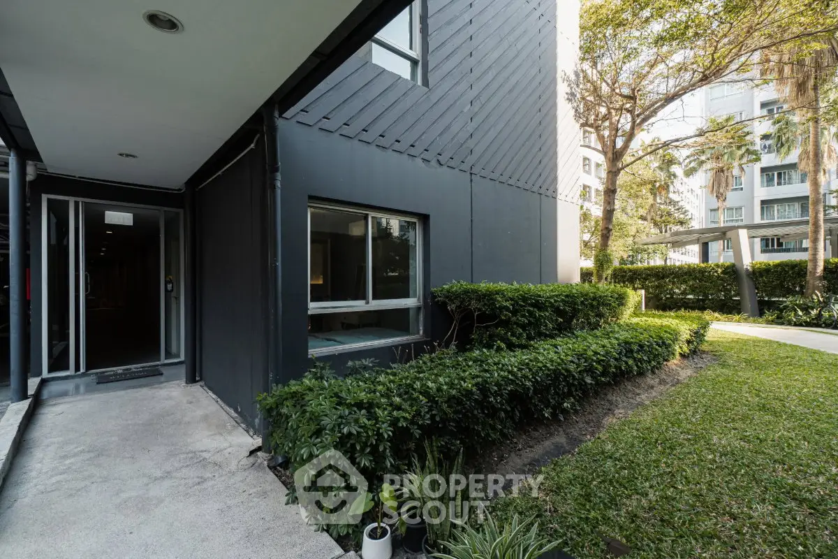 Modern building entrance with lush greenery and sleek architectural design.
