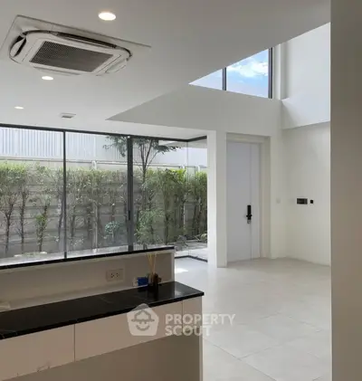 Modern open-layout kitchen with large windows and garden view, featuring sleek design and abundant natural light.