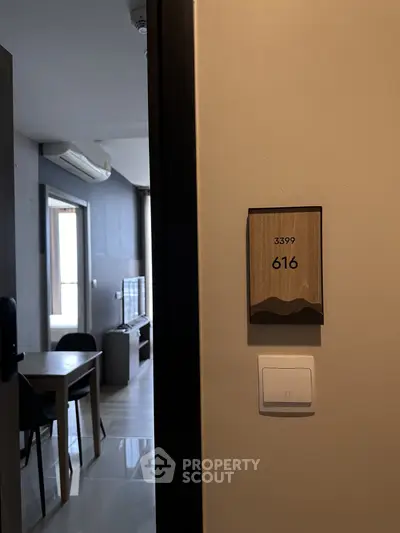 Modern apartment entrance with view into stylish living room featuring dining area and TV.