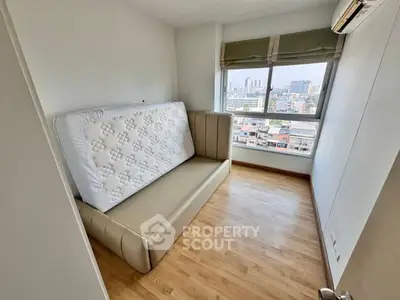 Compact bedroom with city view, featuring a mattress and air conditioning.