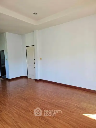 Spacious empty room with wooden flooring and white walls, perfect for customization.