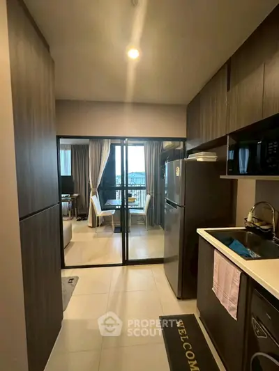 Modern kitchen with sleek cabinets and view into stylish living area with balcony.