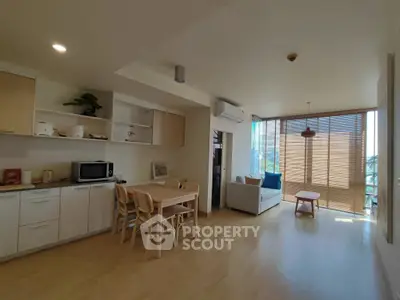 Spacious open-plan living room with dining area and natural light, featuring modern kitchen and cozy seating.