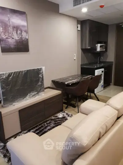 Modern living room with sleek furniture and compact kitchen featuring washing machine and microwave.