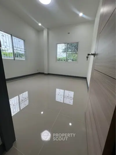 Spacious empty room with glossy tiled flooring and large windows.