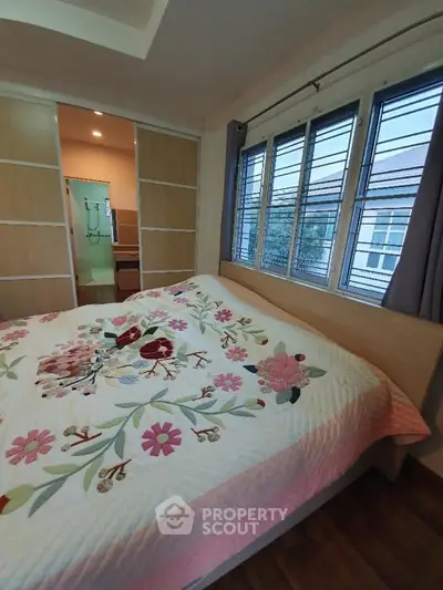 Cozy bedroom with floral bedding and large windows offering natural light.