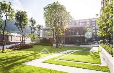 Modern building with lush green garden and pathways in a sunny setting.