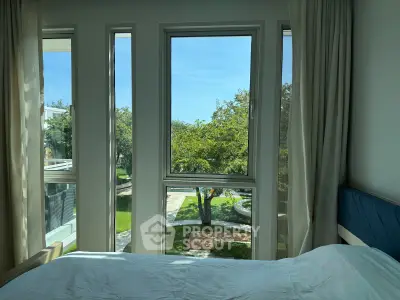 Bright bedroom with large windows offering a serene garden view, perfect for relaxation.