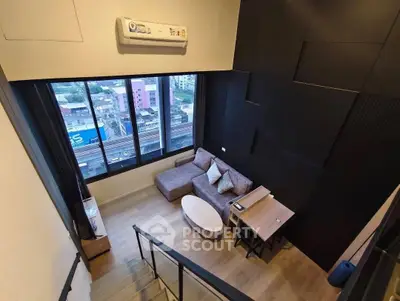 Modern loft-style living room with large windows and city view, featuring cozy seating and sleek design.