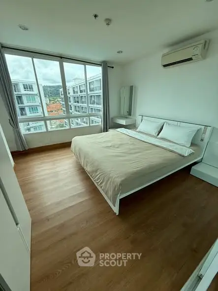 Spacious bedroom with large window and modern furnishings in a high-rise apartment.