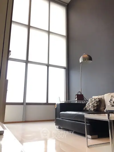 Modern living room with high ceilings and large windows, featuring sleek black sofa and stylish floor lamp.