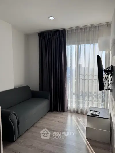 Modern living room with sleek sofa and wall-mounted TV, featuring floor-to-ceiling windows with city view.