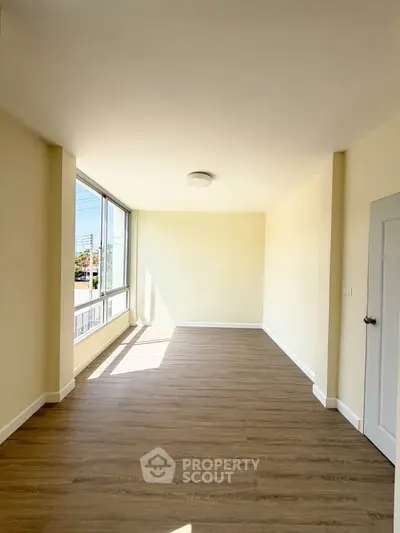 Spacious sunlit room with large windows and wooden flooring, perfect for versatile living space.